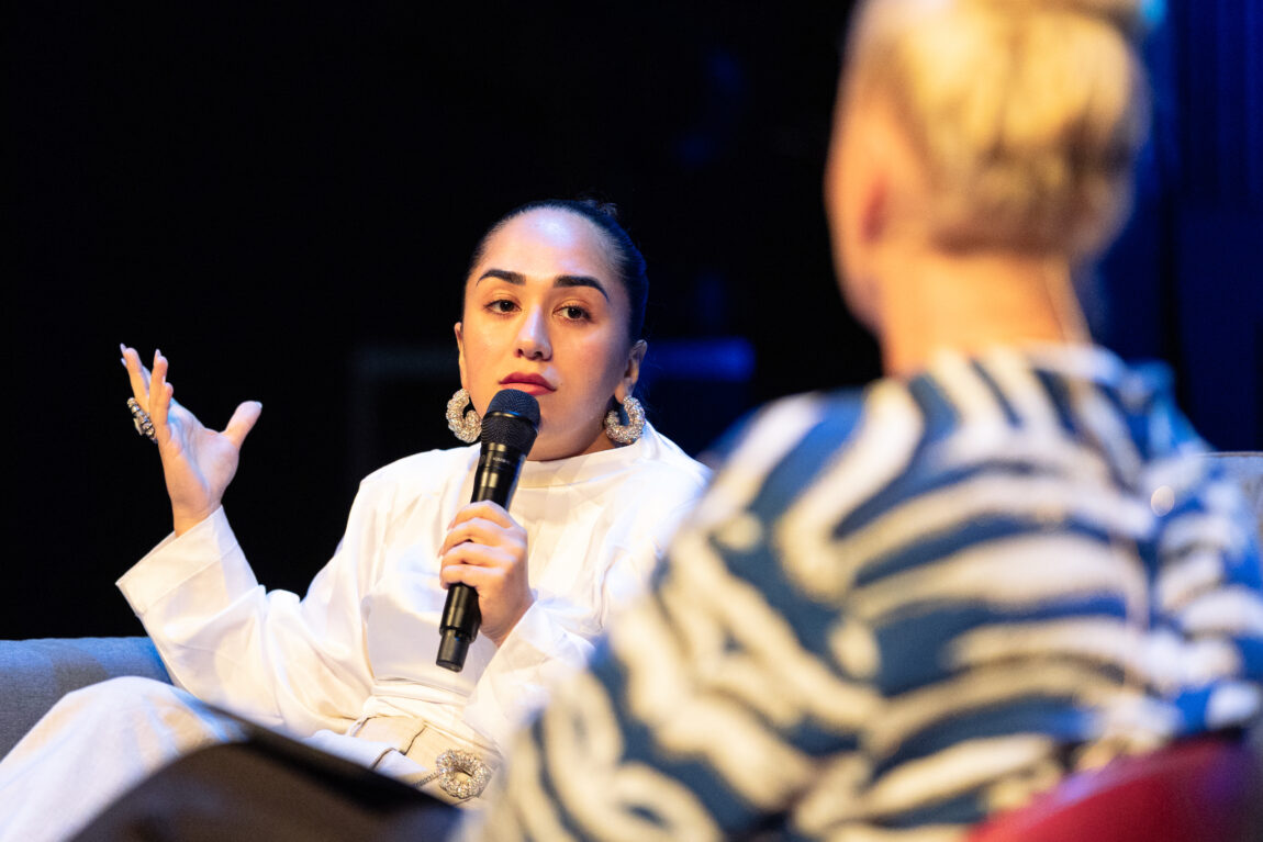 Amanda Delara holder en mikrofon mot munnen. Hun holder venstrehånden opp i været.