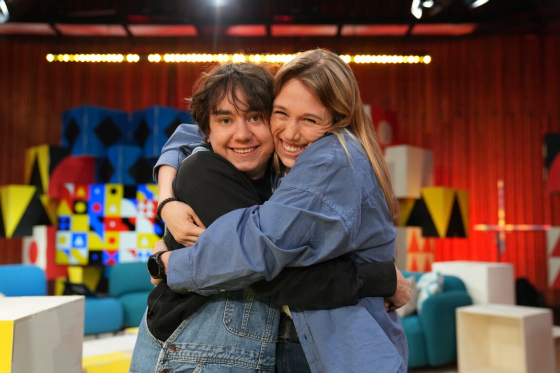 Foto av Henning Bang og Maria Stavang som klemmer hverandre inne i TV-studio. Henning har en svart genser, blå snekkebukse og brunt bustete hår. Maria har en blå skjorte, blondt/brunt hår og smiler bredt med tennene