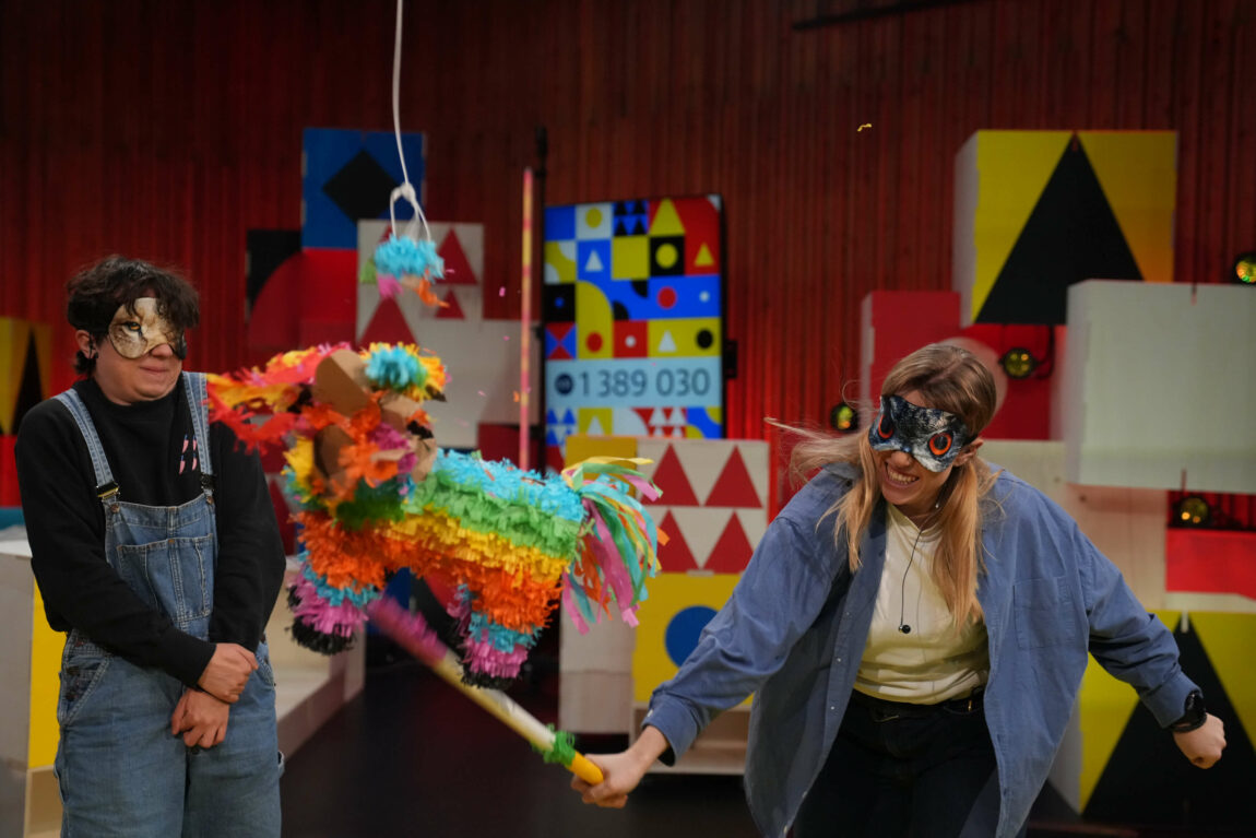 Foto av Maria Stavang som slår en fargerik pinata. Hun har bind foran øynene. Henning står redd i bakgrunnen og blir nesten truffet av pinataen.