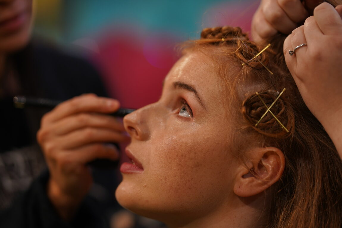 Anna blir sminket. Bildet er tatt fra siden. Hun ser opp for å ikke få eyeliner i øyet.