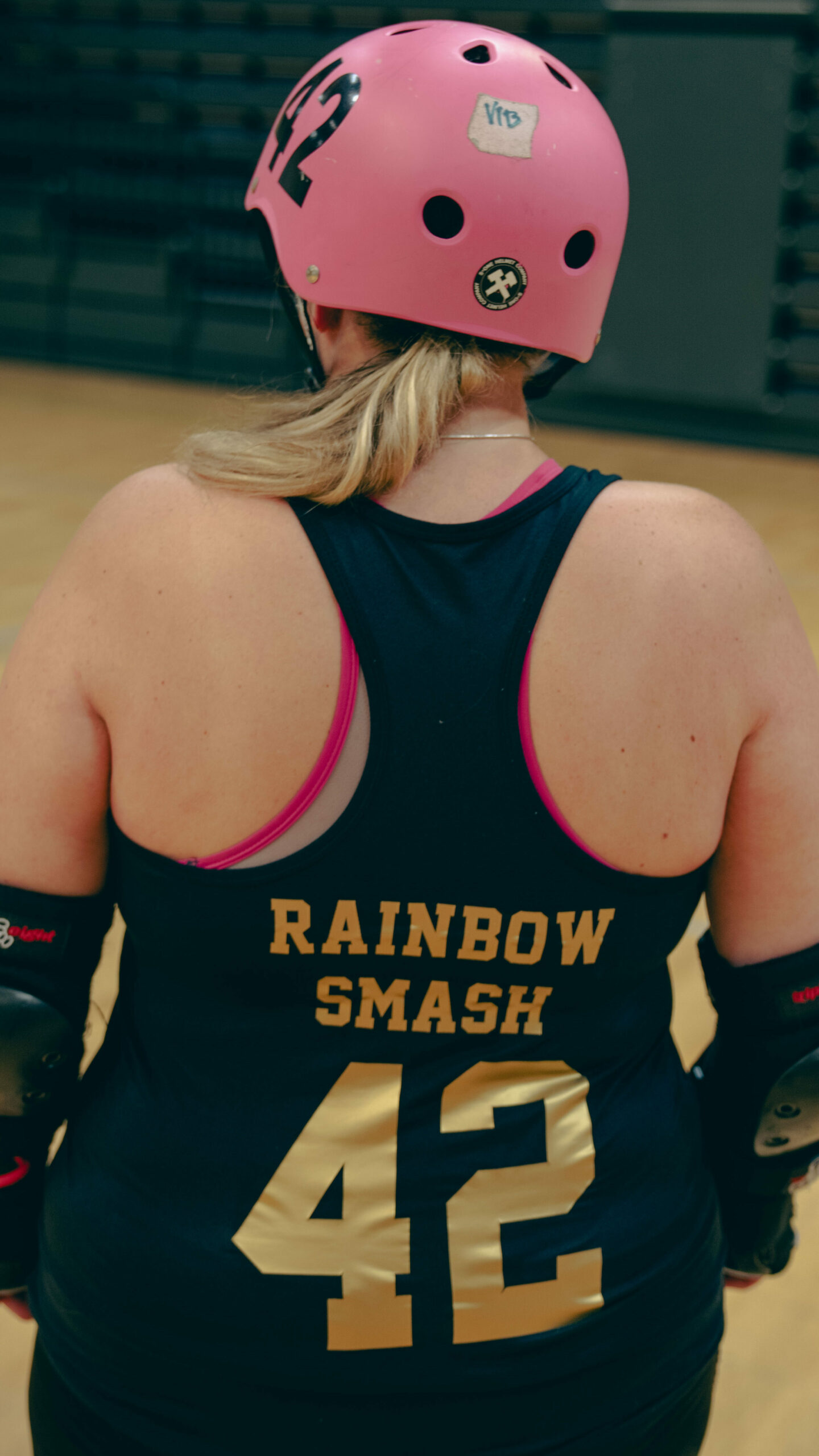 Vibeke står med ryggen til kamera, singleten hennes er i fokus. På den står det skrevet spillernavnet hennes "Rainbow Smash" og spillernummeret hennes 42 i gullskrift. Hun har rosa hjelm, også med nummer 42 på.