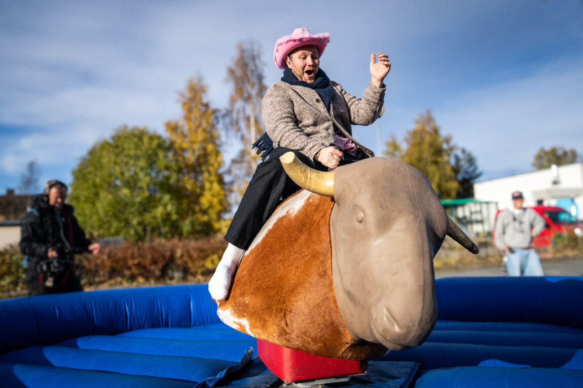 Egil sitter på en mekanisk okse. Han har på seg rosa cowboyhatt. Det er blå himmel.