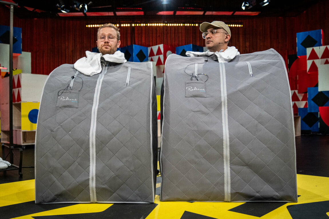 Foto av Egil og Galvan i studio. De sitter i hver sin grå, portable badsstue med et hvitt håndkle rundt halsen. Egil har runde briller og lyst hår. Galvan har beige caps og runde briller. Begge smiler med tennene.