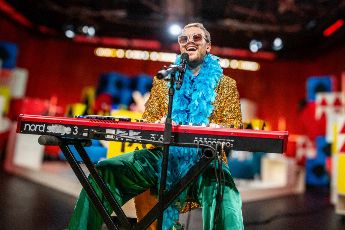 Egil Skurdal har blitt til Elton John, med store glitterbriller, fjærboa, paljettjakke. Han synger fornøyd bak keyboardet.