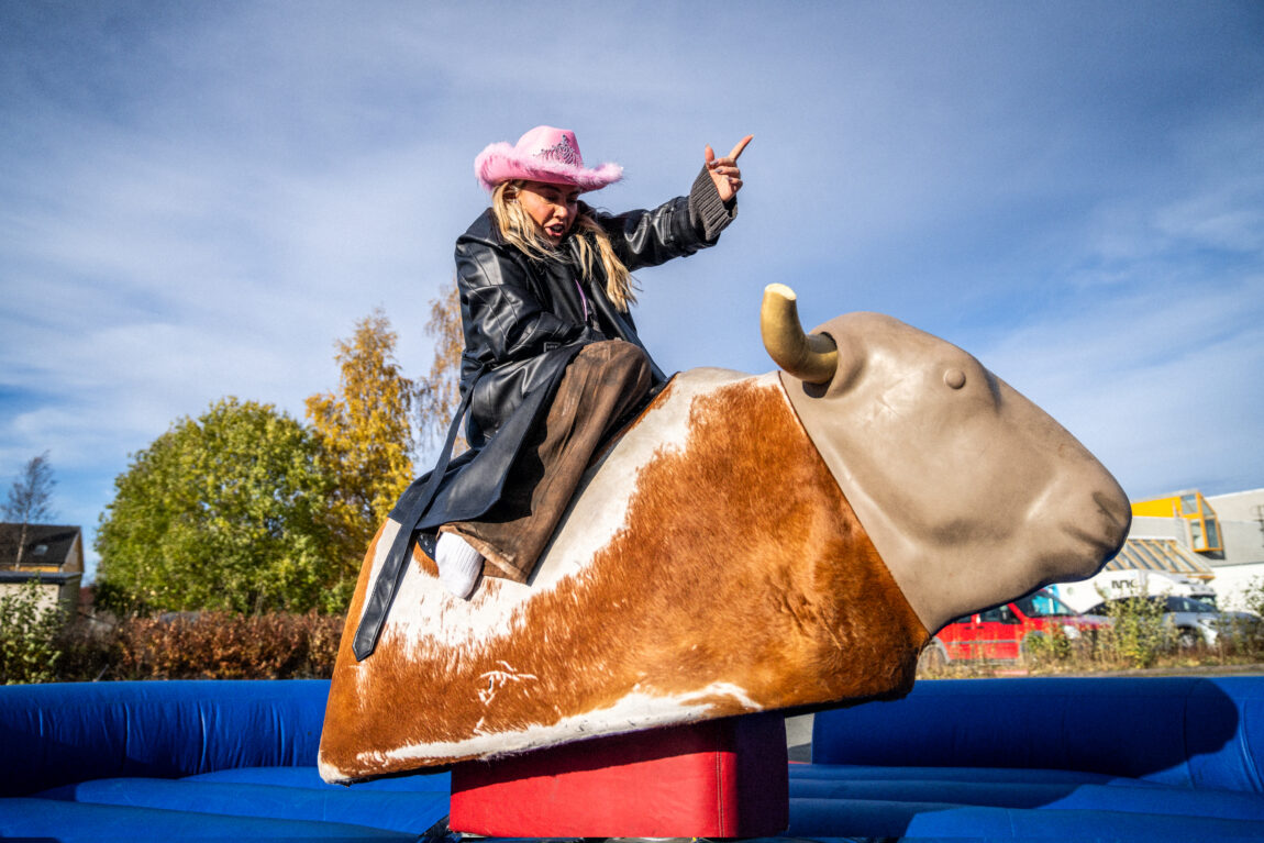 Julie sitter på en mekanisk okse. Hun har rosa cowboyhatt. Det er blå himmel.