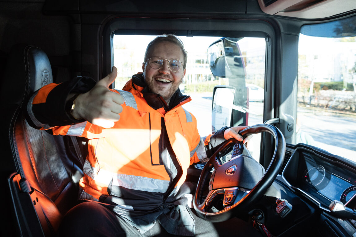 Egil sitte ri førersetet på en lastebil. Han har oransje jakke og viser tommel opp og smiler. 