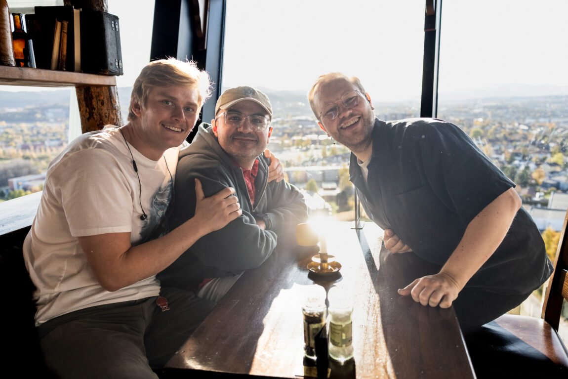 Karsten, Galvan og Egil sitter rundt et bord. Bak dem er det vindu med utsikt over hus i Trondheim. Det er sol inn der de sitter.