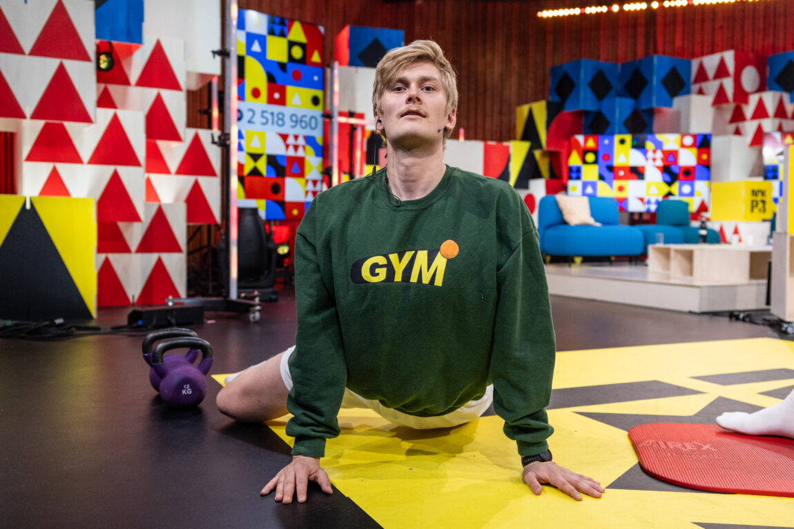 Karsten ligger på bakken rettet mot kamera med ene kneet ut. Han har på seg en grønn genser det står gym på.