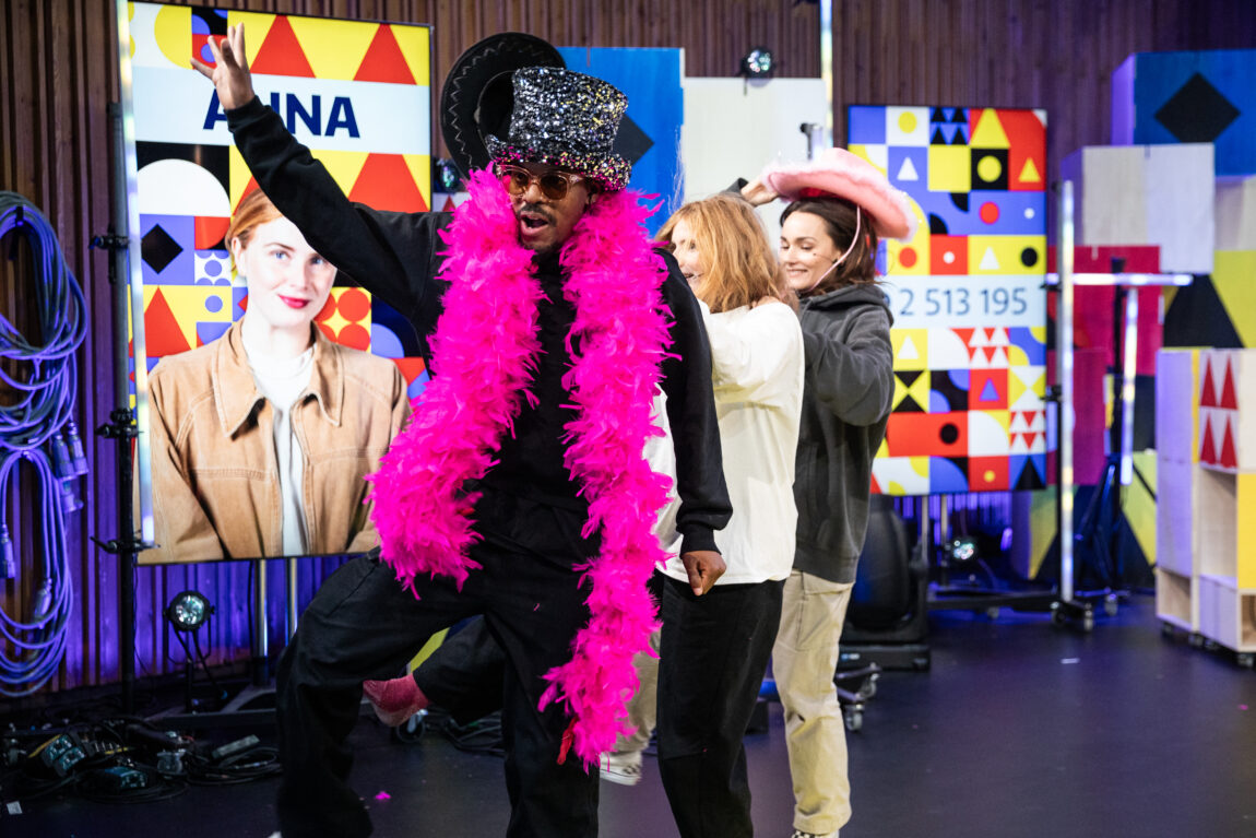 Nate, Anna og Arian danser. Nate har på seg rosa fjærskjerf og glitterhatt, og Arian har på seg rosa cowboyhatt.