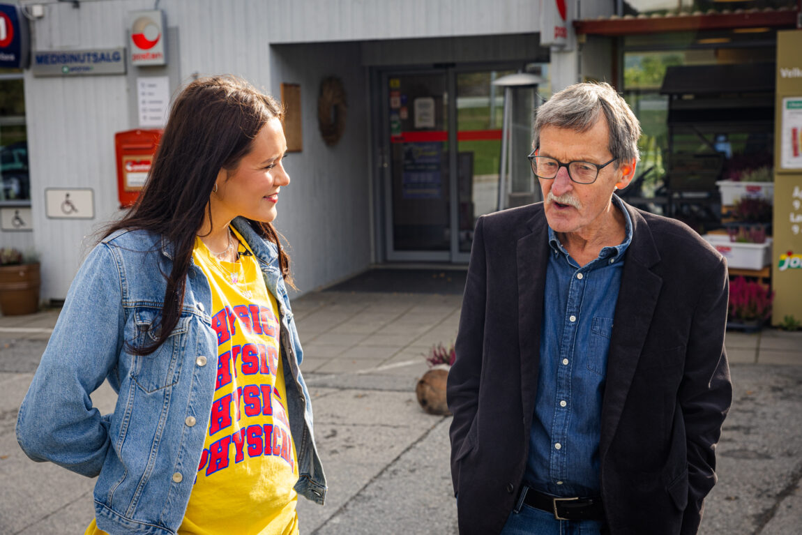 Synne har på seg en ola-jakke og en gul t-skjorte. Hun smiler og ser på Paul-Gunnar som har på seg en blå skjorte og en svart dressjakke. 