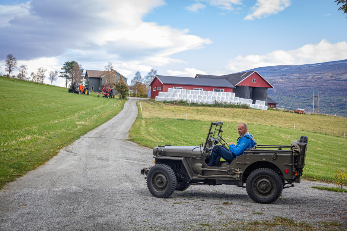 Paul Gunnar sitter i en gammel Jeep. Bak han ser vi en gård med hvite høyballer. 