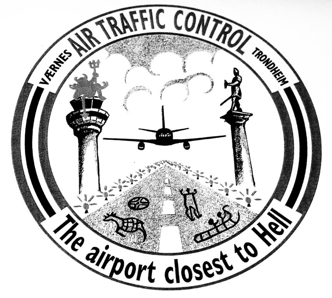 Nærbilde av et stempel/klistremerke. Det er rundt, tegningen i midten viser et fly på vei til å lande på rullebanen. I tekst rundt står det "Værnes Air Traffic Control Trondheim", "The airport closest to Hell"