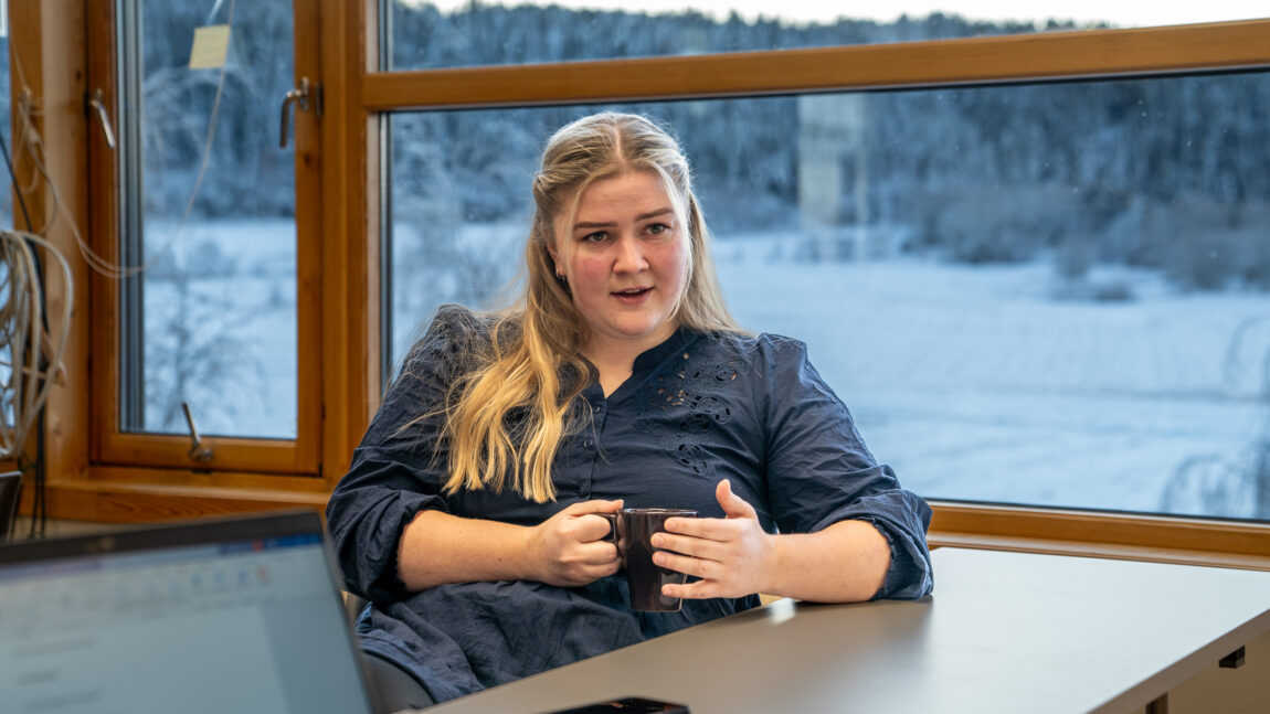Birgit har et nøytralt uttrykk som grenser over til alvorlig, hun sitter og holder rundt en kaffekopp. Ut vinduet bak henne er det full vinter.