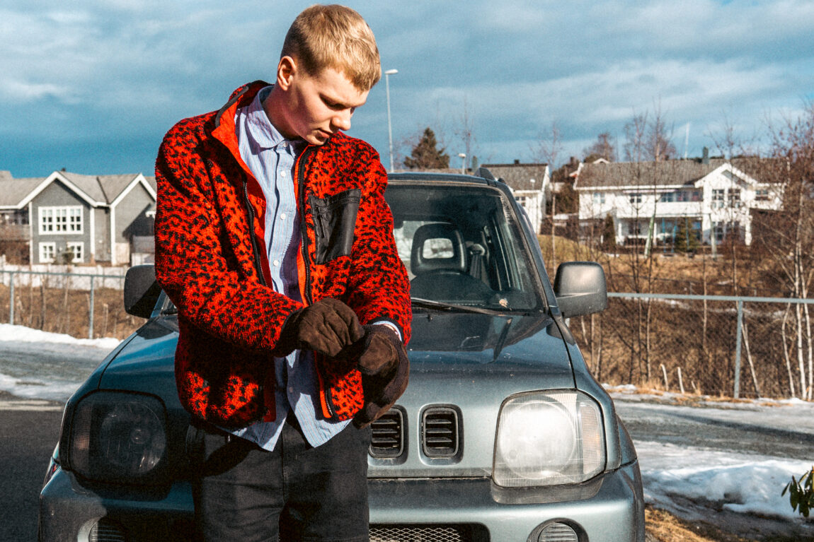 Ung mann som poserer foran en gammel bil. Han ser ned på hendene, mens han tar på seg hanskene sine. 