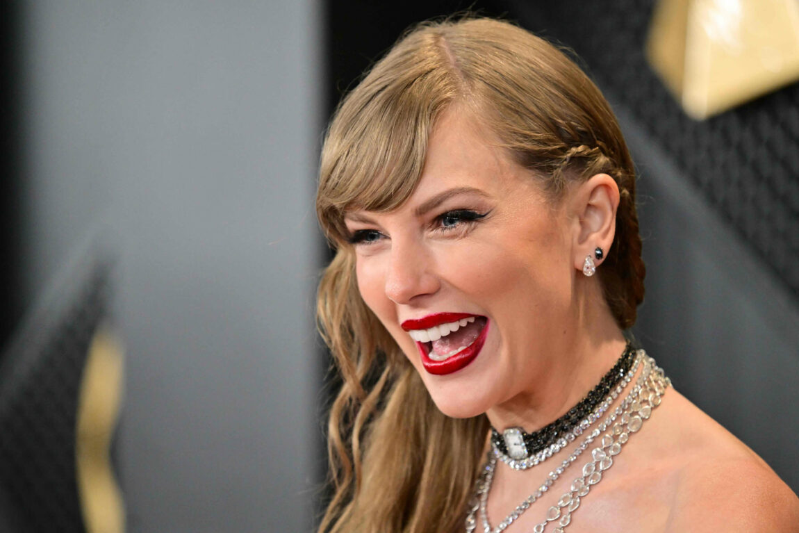 Et nærbilde av Taylor Swifts fjes. Hun ler. Hun har på mange smykker rundt halsen.