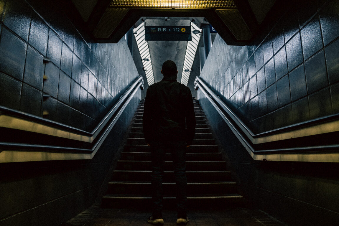Bildet viser trappa på en t-banestasjon. I midten av trappa står en mann med ryggen til. Det er mørkt. 
