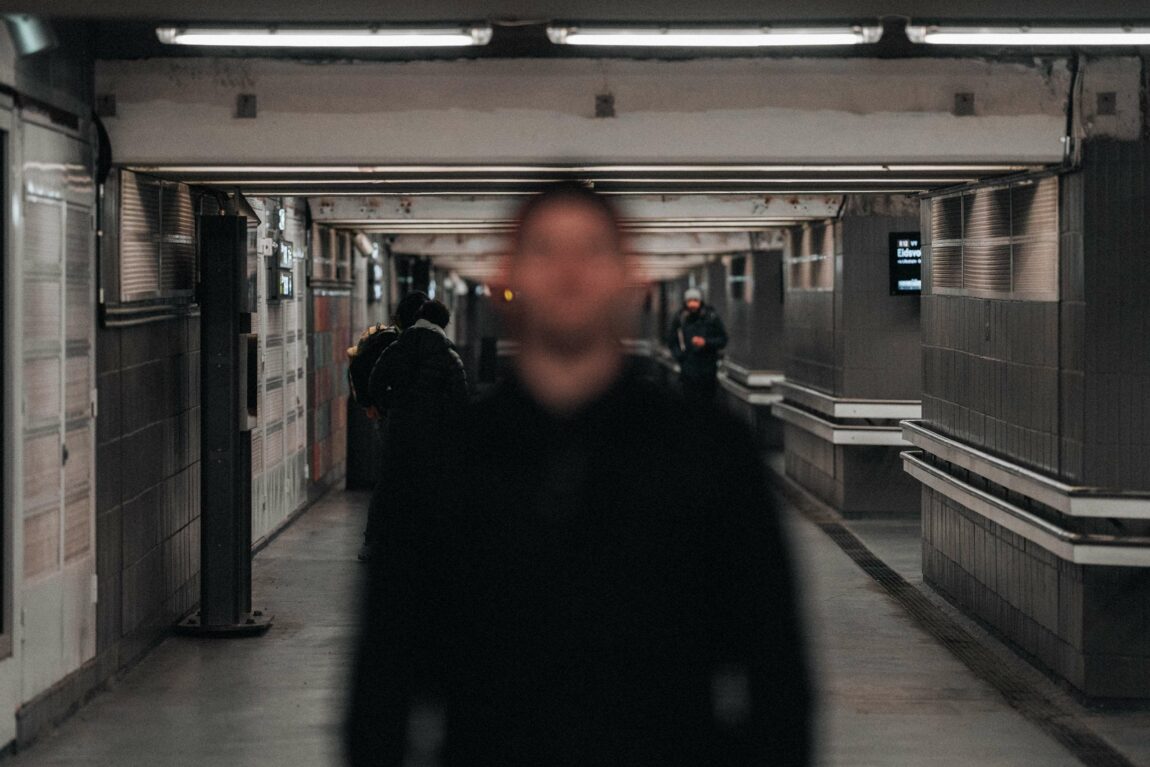 Bildet viser en mann som står nede i en t-banetunnel. Han er blurry, så man ser ikke ansiktet hans tydleig. I bakgrunnen ser man flere andre mennesker. 