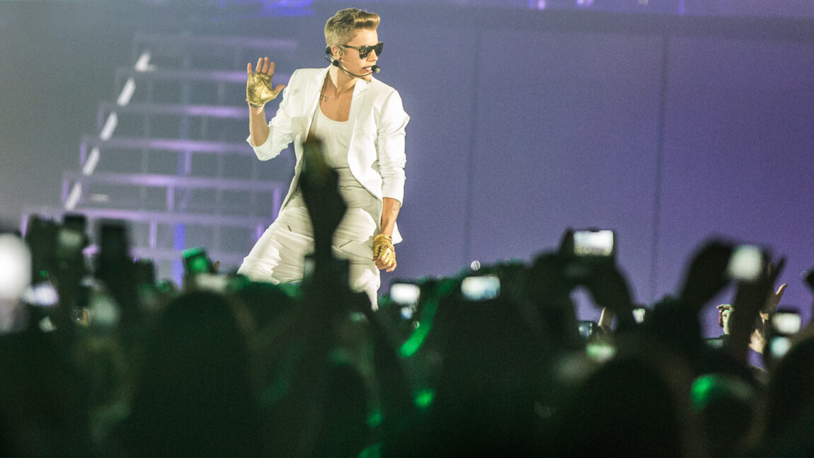 Justin Bieber har på seg en hvit dressjakke og t-skjorte og har på seg gullhansker, mens han synger og shower.