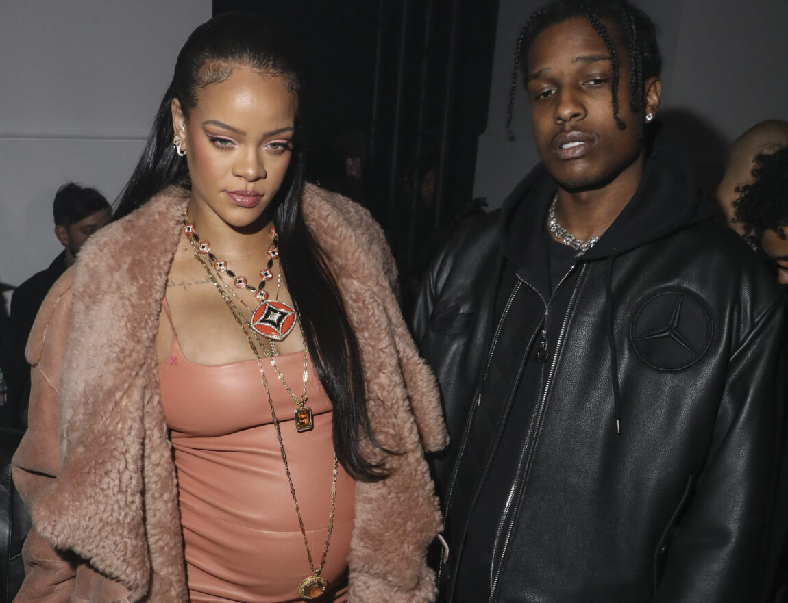 Rihanna og Asap Rocky står ved siden av hverandre. Rihanna er gravid og har på seg en oransje kjole med en pelskkåpe rundt. Asap Rocky har på seg en svart skinnjakke.