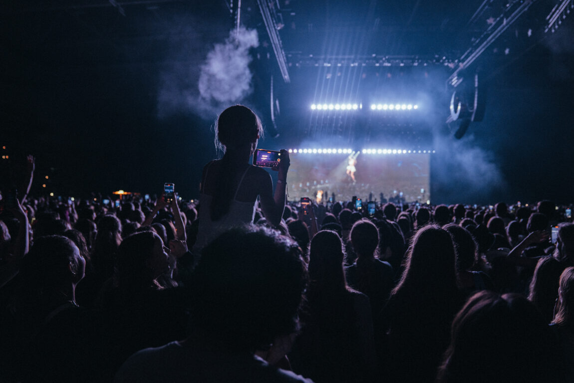 Mange unge jenter står fremfor en scene. Det er mørkt og røyktfylt i konsertsalen og man ser vagt en kvinne danse på scenen langt der fremme. 