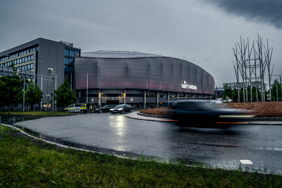 Et bilde av Unity Arena på kvelden. Vi ser biler som kjører rundt en rundkjøring. Og logoen til Arenaen i det fjerne.