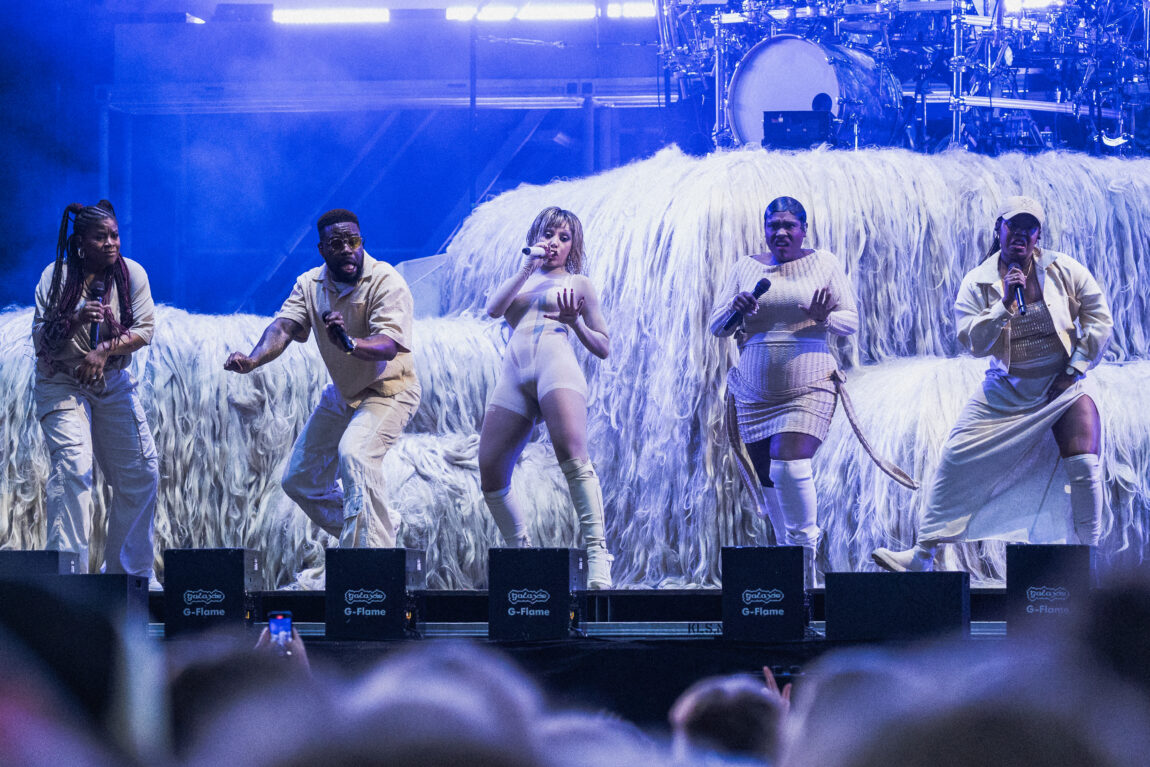 Doja Cat spiller med masse dansere ved siden av hun. Bak der er det en trommeslager.