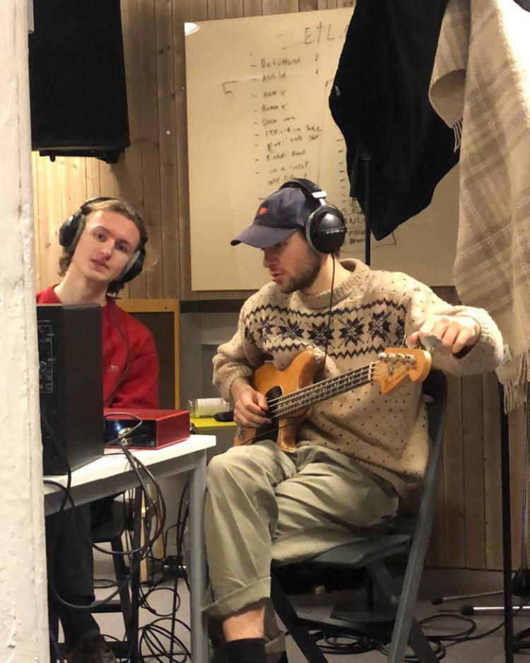 To av medlemmene i Uironisk Distanse stemmer en gitar i et studio. 