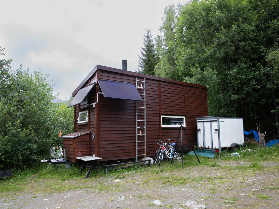 Minihuset er mørkebrunt og har eit smalt vindauga på langsida. Det er ein stige festa på veggen og solcellepanel på enden.