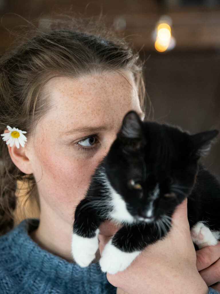 Anna held opp katten til ansiktet hennar, slik at halve fjeset hennar er skjult bak ho. Ho ser til sida alvorleg og har ein prestekrage bak eine øyra.