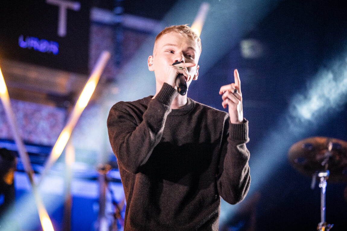 Anakin Justin har på seg en brun genser og rapper og hoier