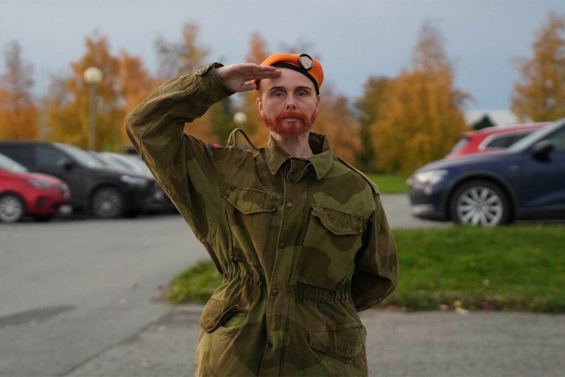 Anna Nor Sørensen har blitt forvandlet til fenriken fra Kompani Lauritzen. Hun har på seg militæruniform og oransje beret, og har fått oransje skjegg i ansiktet.