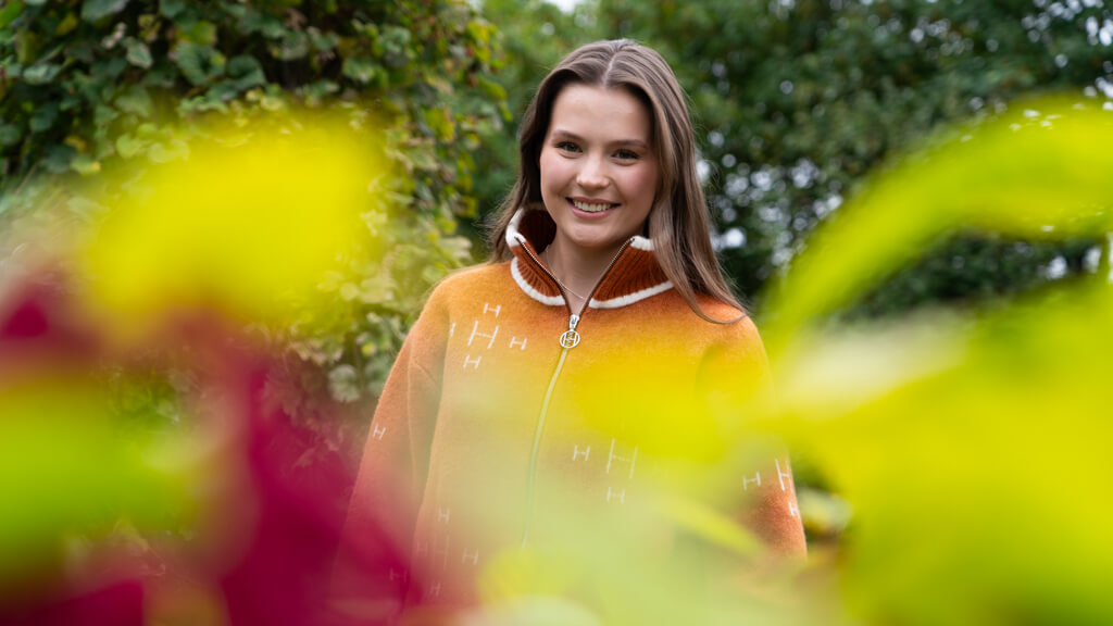 Emma smiler til kamera. Hun har på seg en oransje strikkagenser.