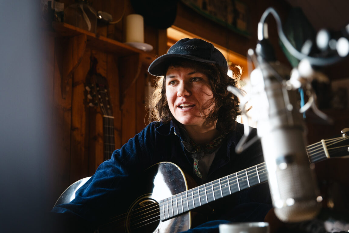 Fay Wildhagen sitter og jobber med en gitar. HUn har på seg en svart caps.