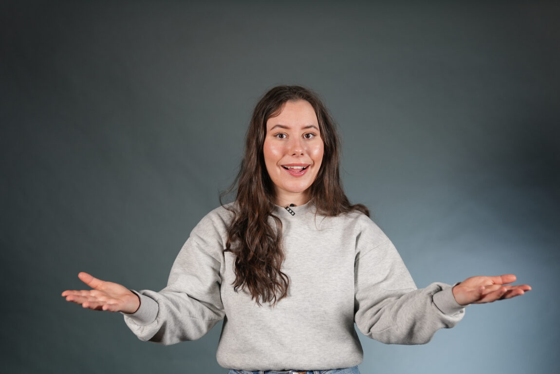 Katarina har hendene ut til værs og har en grå genser langarmet.