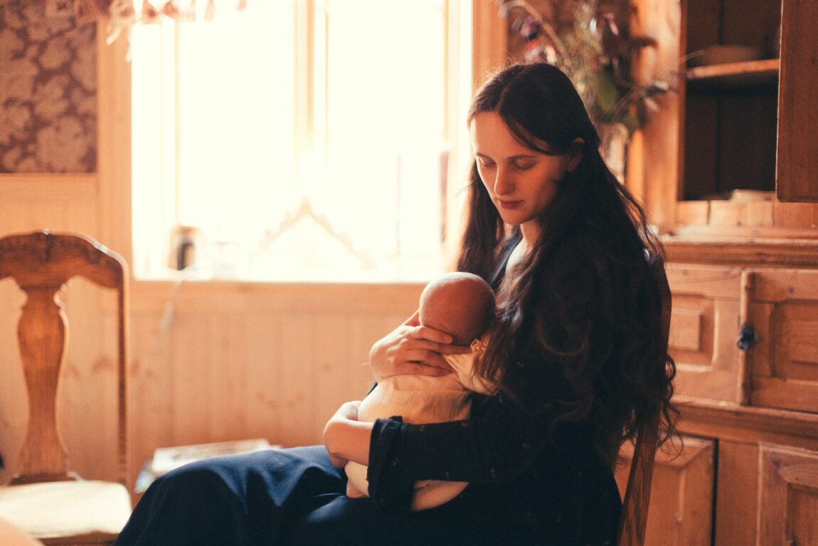 Aftur sitter på en trestol og holder sin nyfødte baby i armene.