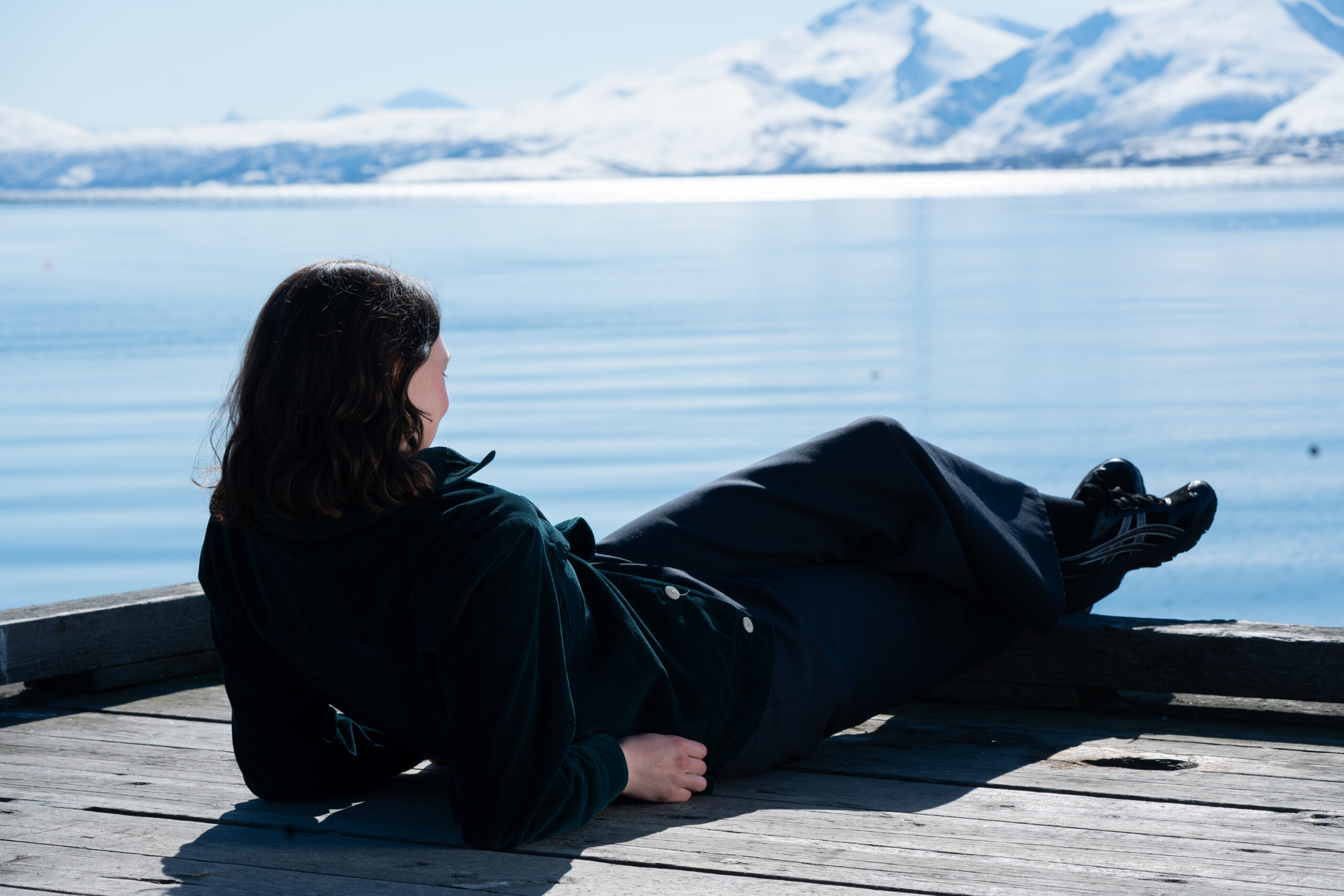 Stéphanie Turcotte ligger på en brygge med blikket mot vannet og fjellene.