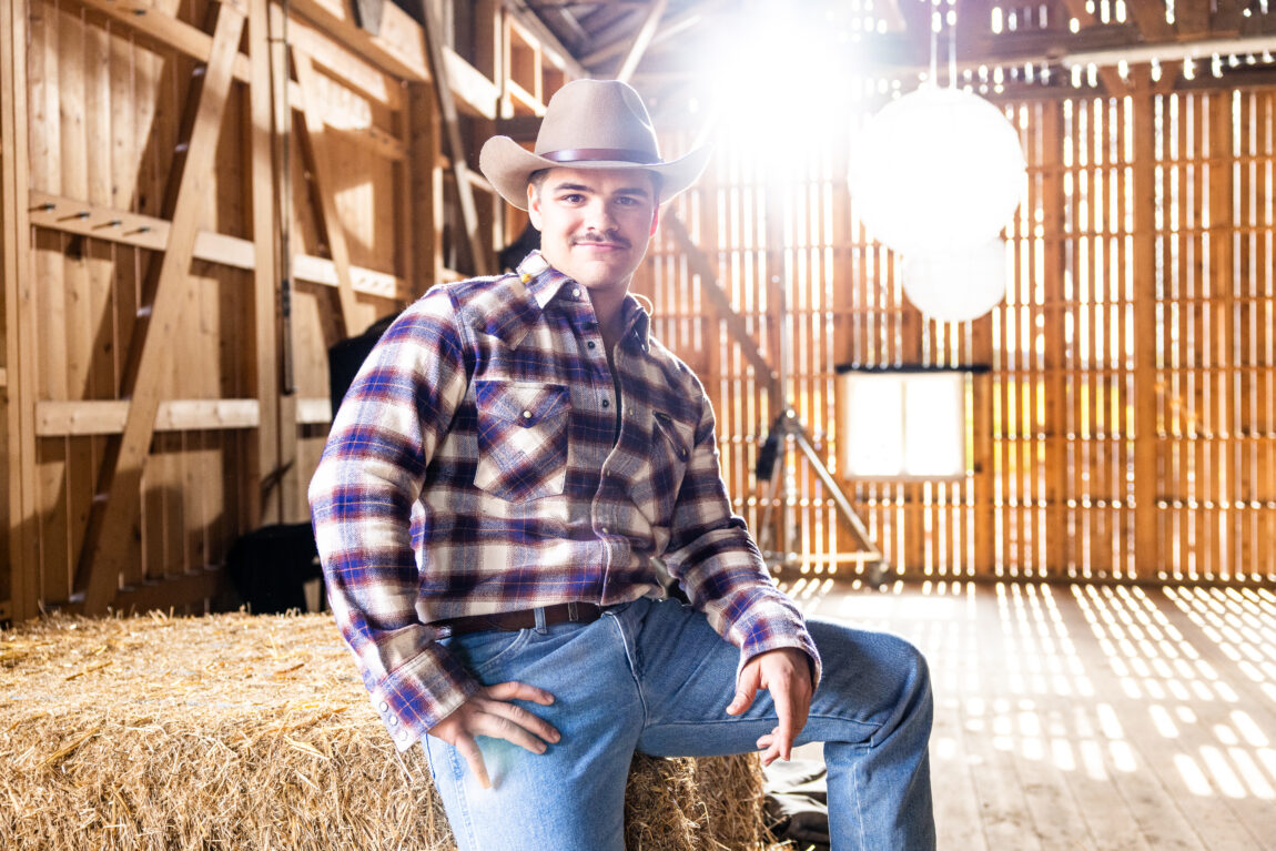 Tobias SteN har på seg en rutete skjorte, cowboyhatt og stirrer forfjamset inn i kamera. Han sitter på et høy.