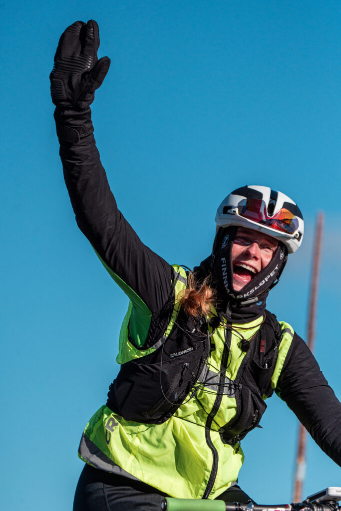 Anna vinker glisende til kamera med gul sykkelvest og svarte hansker.