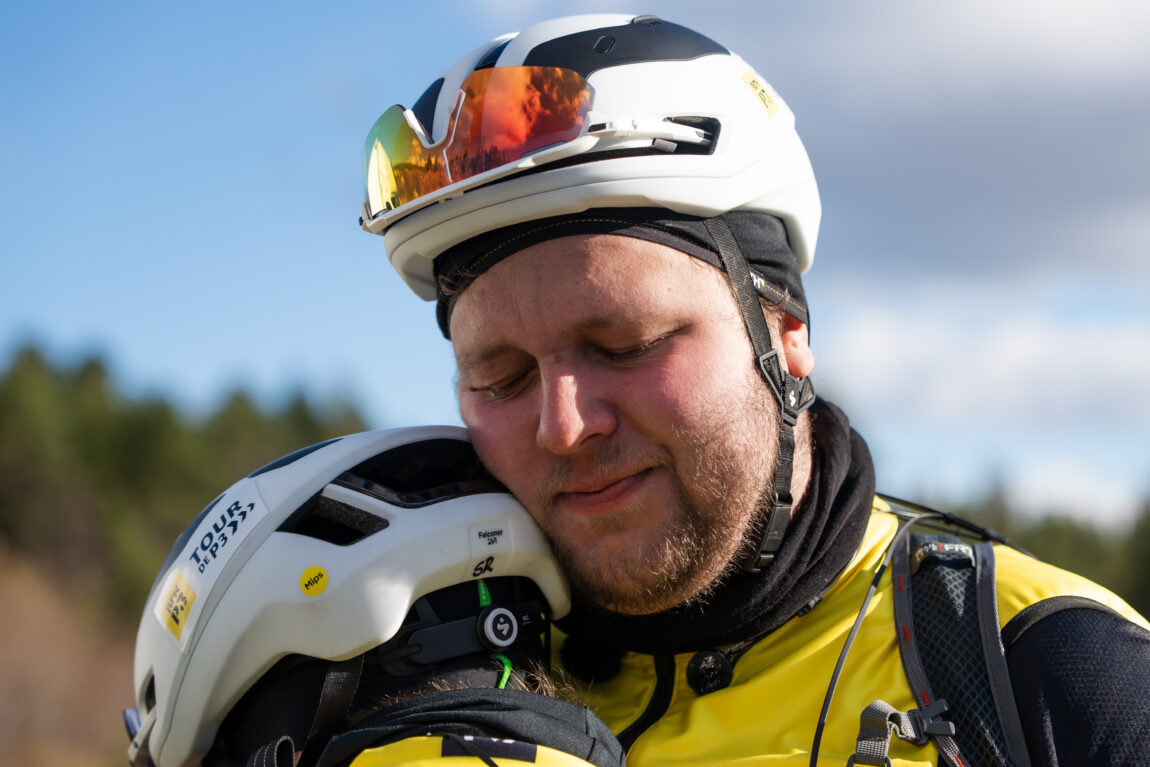 Jonas er tydelig prega idet han får en klem av Sindre, begge har på hvite sykkelhjelmer.