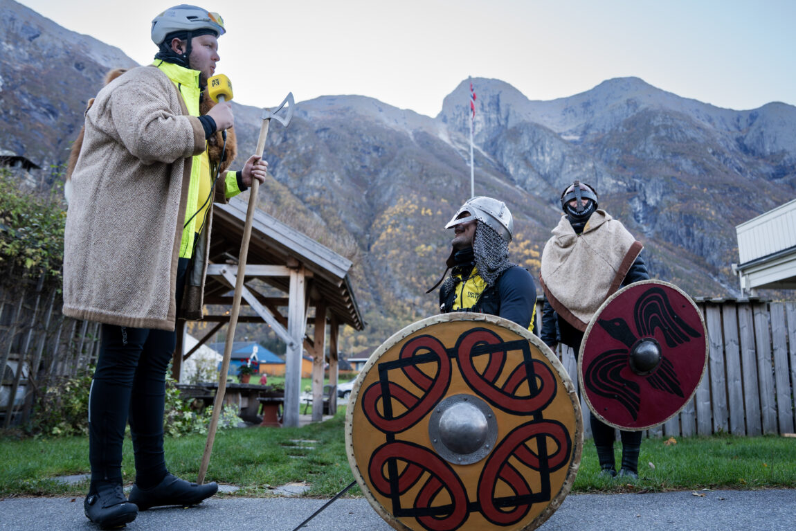 Jonas står over en sittende Sindre med øks og P3-mikrofon i hånda. Sindre har på seg vikinghjelm og skjold. Anna står med vikinghjelm og skjold i bakgrunnen.