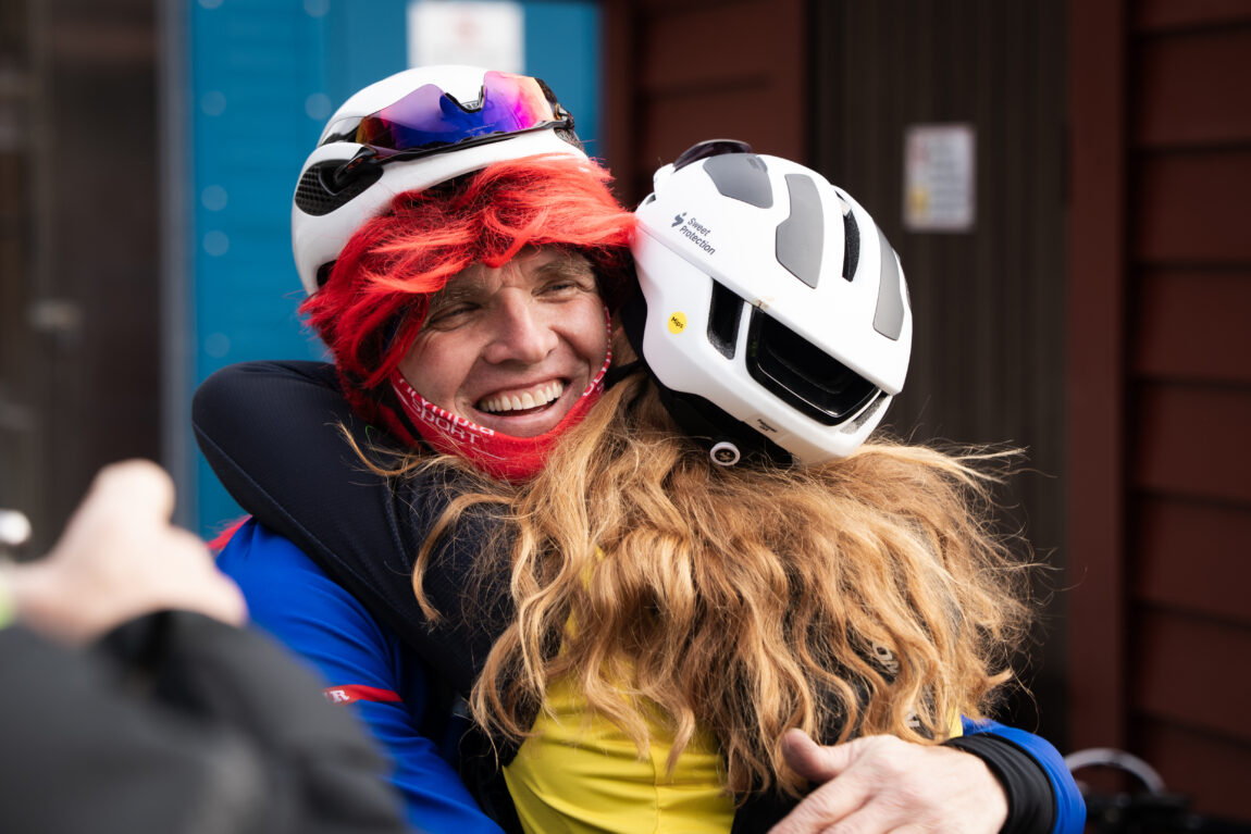 Anna gir en mann med rød parykk under sykkelhjelmen en klem.