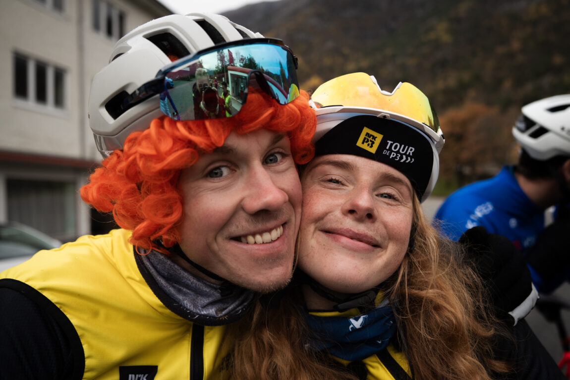 Carl Fredrik og Anna smiler til kamera, Carl Fredrik har på seg rødhåra, krøllete parykk under hjelmen.