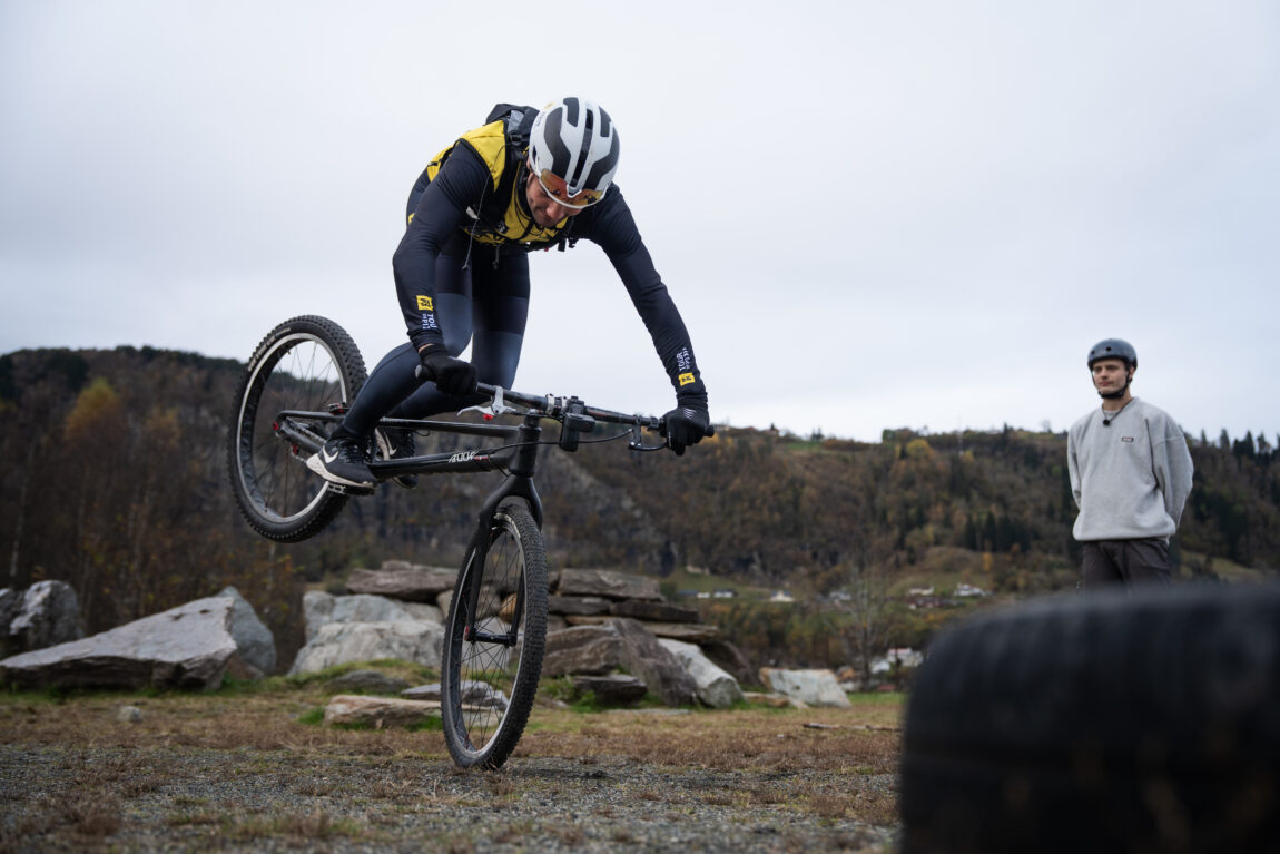 Sindre steiler på bakhjulet og stuper nærmest over styret, trener Eirik er i bakgrunnen.