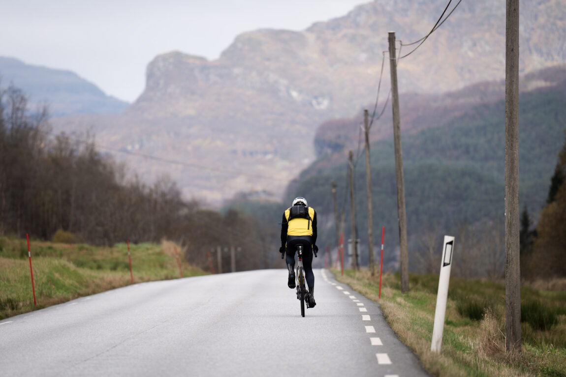 Ryggen til Sindre på sykkelsetet en siste gang før Bergen, foran han er store, høstfargede, nesten lilla, fjell.