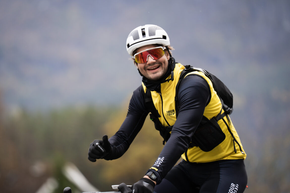 Sindre smiler og viser tommel opp til kamera ikledd solbriller, sykkelvest og sykkelhjelm.