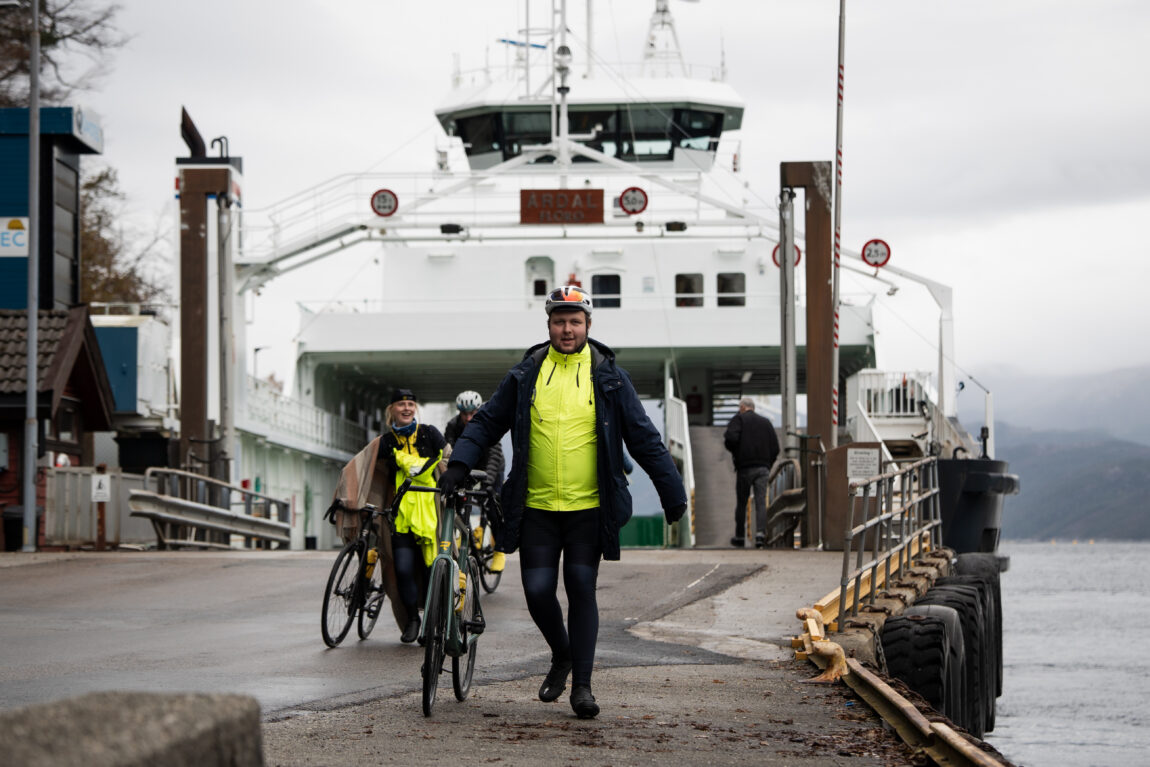 Jonas triller sykkelen av ferga ikledd blå parkas over den gule sykkeljakka.