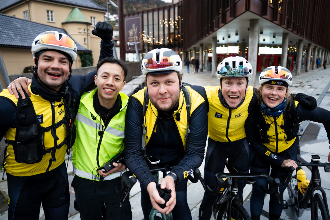 Fem glisende syklister og produsenter gliser inn i kamera.