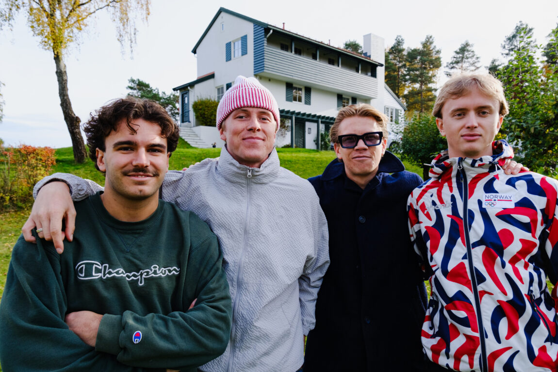 Nærbilde av gutta i Golf. De holder rundt hverandre og smiler. Bak dem er det et hvitt hus.